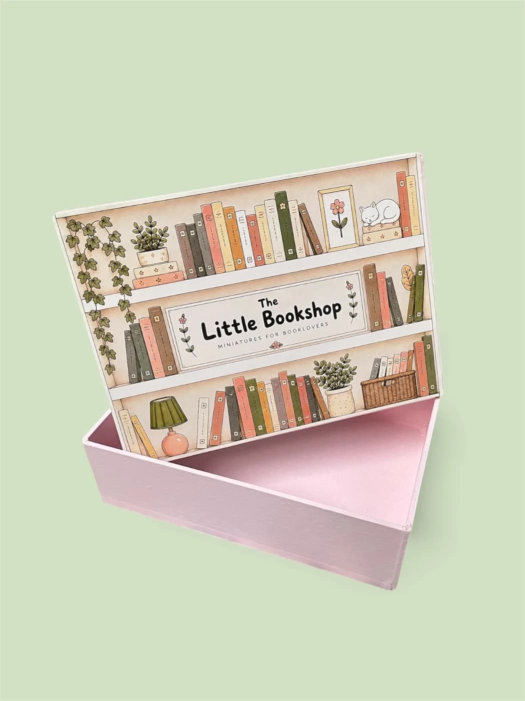 The Little Bookshop gift box open on a sage green background, its illustrated bookshelf lid propped behind
